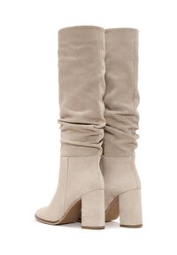 Bottes en suede beige montantes avec un design froncé, bout carré et talon épais. Comprend une fermeture éclair sur le côté pour un enfilage facile.