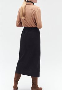 Blusa marrone a maniche lunghe abbinata a una gonna nera lungo caviglia; tessuto testurizzato, vita arricciata, completata da stivali marroni al ginocchio.