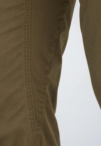 Olivengrønt bomuldsstof med en glat tekstur og synlige sømdetaljer; beskåret udsigt fokuserer på siden af et tøj.