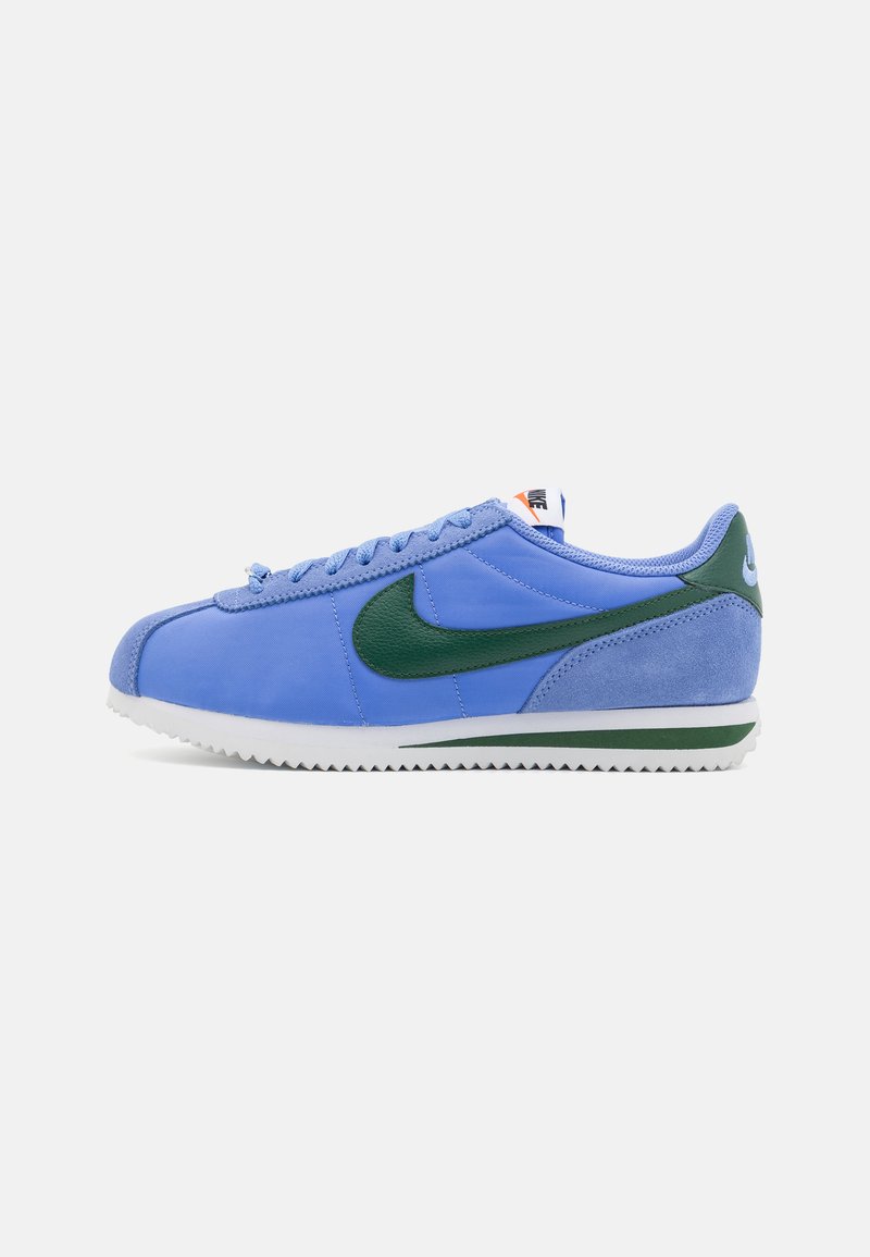 Kék szövetből és velúrból készült sneaker, zöld Nike logóval, fehér talppal és textúrázott talprésszel. Cipzáras dizájnja és párnázott cipőgallérja van.
