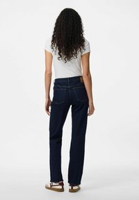 Zila denima džinsi ar taisnu kāju un piecu kabatu dizainu, apvienoti ar baltu pieguļu t-kreklu un daudzkrāsainiem sporta apaviem.