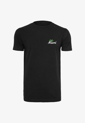 Juodas medvilninis trumpomis rankovėmis marškinėliai, kuriuose yra baltas „Miami“ logotipas ir žalias palmės dizainas kairiajame krūtinės srityje.