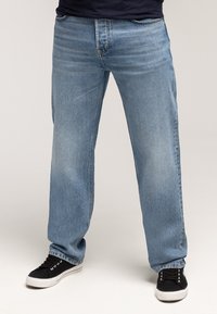 Jasnoniebieskie dżinsy z denimu o luźnym kroju, prostych nogawkach, detalach postarzenia i klasycznym pięciokieszeniowym fasonie, zestawione z czarnymi trampkami.