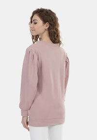 Felpa a maniche lunghe rosa chiaro con maniche a sbuffo, scollo rotondo e orlo a coste. Il tessuto sembra morbido e leggermente texturizzato.