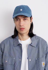 Boné de algodão azul com um pequeno logótipo, jaqueta listrada em azul-marinho e branco, e camiseta branca. Apresenta um design simples e um ajuste descontraído.
