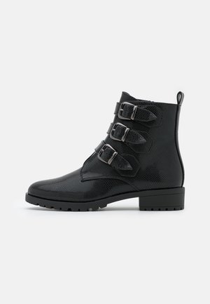 Bottine noire texturée à cheville avec trois sangles à boucle argentée, semelle robuste, petit talon et languette à l'arrière.