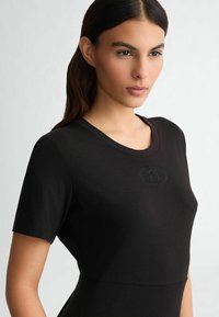 Black fitted t-shirt with short sleeves, featuring a crew neckline and embossed logo detail. Made from smooth, stretchy fabric.