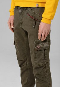 Olivgrüne Cargo-Hosen mit Front- und Seitentaschen, Reißverschlusselement und Stoff-Logo-Label. Hergestellt aus strukturiertem Baumwollmaterial.
