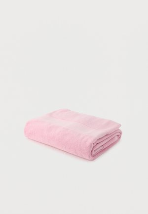 Serviette douce rose pliée avec une bande lisse, posée à plat sur une surface blanche.