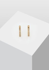 Boucles d'oreilles en métal doré avec un design droit, comportant une rangée de cristaux transparents sur un côté. Fini métallique lisse et texture polie.
