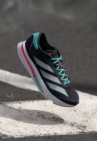 Zwarte sportieve schoen met lichtblauwe accenten, synthetisch bovenwerk, drie witte strepen en een gestructureerde zool. Kenmerkt felle roze details.