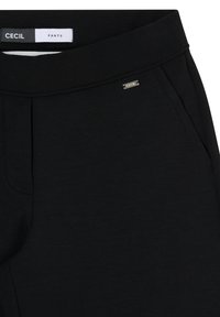 Ceinture de pantalon noire avec une étiquette cousue "CECIL" et une petite plaque métallique de la marque sur le côté droit près de la poche.