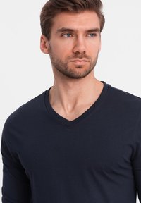 Langärmliges T-Shirt in Marineblau mit V-Ausschnitt, aus weichem Stoff gefertigt. Verfügt über eine taillierte Silhouette und eine glatte Textur.