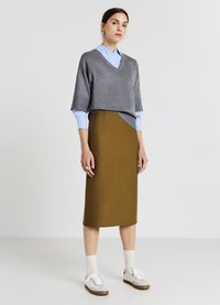 Grauer, kurzärmeliger Pullover über einem hellblauen Hemd, kombiniert mit einem braunen Bleistiftrock und weißen Sneakern mit grauen Akzenten.