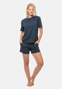 Donkerblauwe katoenen T-shirt met korte mouwen, gecombineerd met polkadot shorts in marineblauw en wit, met een elastische tailleband en zakken.