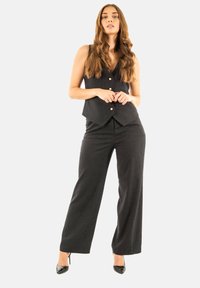 Conjunto de chaleco y pantalones de rayas negras, con escote en V, cinco botones y pantalones de pierna ancha, combinado con tacones negros de punta.