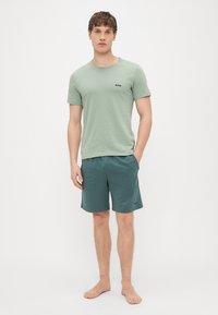 T-shirt de algodão verde claro com um pequeno logótipo preto, combinado com calções desportivos verde escuro. Ajuste casual, mangas curtas e design minimalista.