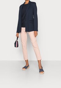 Blazer blu marina sopra un maglione blu marina, abbinato a pantaloni cropped rosa chiaro e espadrillas blu. Piccola borsa blu marina con un accento a strisce rosse e bianche.