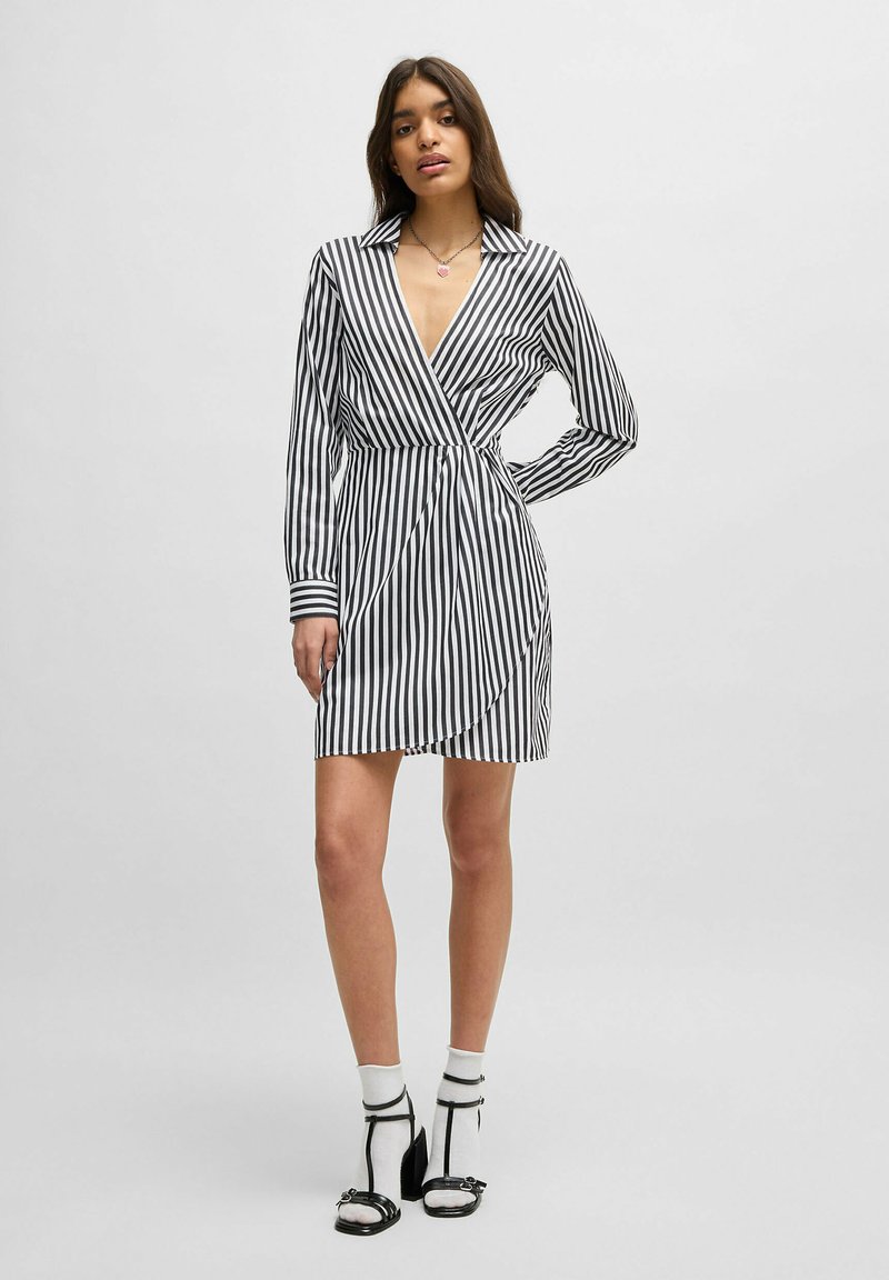 Zwart-witte gestreepte wikkeljurk met lange mouwen, een kraaghalslijn en een strik in de taille. Heeft een lengte tot halverwege de dij.
