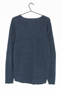 Långärmad skjorta i marinblått, tillverkad av strukturerad tyg, med en vid halsringning och en böjd fåll. Hänger på en svart metallkrok.