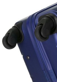 Blue hard-shell suitcase with textured surface, black wheels, and zipper. Features a sturdy design with rounded edges and reinforced corners.