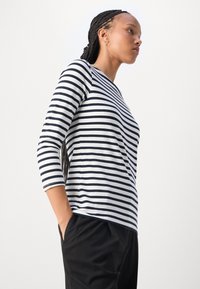 Langärmliges T-Shirt mit Rundhalsausschnitt in navyblau-weißen horizontalen Streifen, aus weichem Stoff, kombiniert mit schwarzen Hosen.