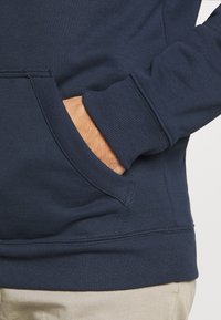 Mörkblå sweatshirt med ribbad mudd och nederkant, samt en framficka i kängurustil. Materialet verkar mjukt och texturerat.