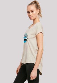 Beige short-sleeve t-shirt with a rounded neckline and a graphic print featuring blue and black accents. Soft, lightweight fabric.