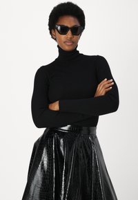 Suéter negro de cuello alto acanalado combinado con una falda A de charol negro con estampado de cocodrilo. Modelo usando gafas de sol oscuras de ojo de gato.