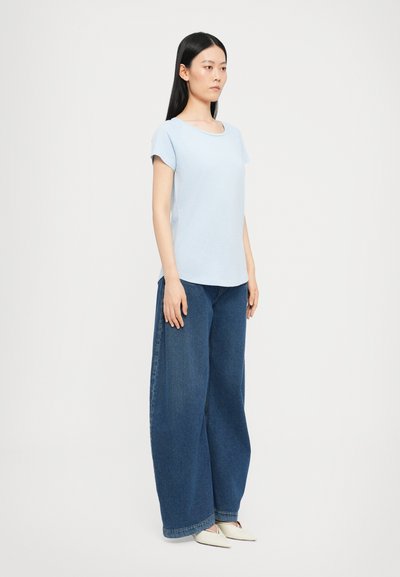 Light blue short-sleeve t-shirt with a rounded neckline, paired with wide-leg dark blue jeans, displayed on a model against a plain background.