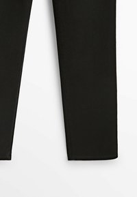 Pantalon noir à coupe droite, visible de la mi-cuisse à l'ourlet, sur un fond blanc uni.
