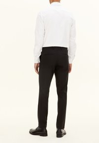 Weißes Langarmhemd, schwarze Slim-Fit-Hose, glattes Material, geknöpfte Manschetten, klare Linien, kombiniert mit schwarzen eleganten Schuhen.