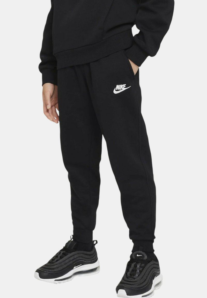 Pantalones de chándal negros con cintura elástica, bolsillos laterales y logotipo de Nike en blanco en la pierna izquierda, combinados con zapatillas negras.