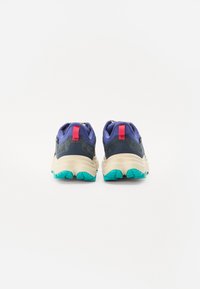 Scarpe da trail running con tomaia viola, dettagli neri e suola crema. Evidenziate da una suola teal con una linguetta rossa sul tallone e un design testurizzato.