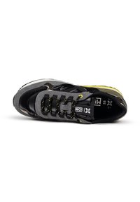 Zapatilla negra y gris con una superficie texturizada, acentos amarillos y cordones negros llamativos. Incluye un diseño con paneles laterales distintivos y logo.
