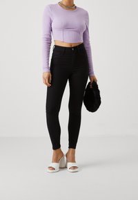 Lila ribbad långärmad crop top, högmidjade svarta skinny jeans, vita platåklackar och en svart fluffig väska.