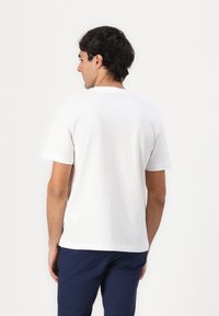 Hvid bomulds T-shirt med rund halsudskæring og korte ærmer, med et enkelt design og afslappet pasform, båret med marineblå bukser.