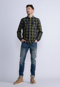 Karierter Flanellhemd in Dunkelblau und Grün mit zwei knöpfbaren Brusttaschen. Getragen mit ausgewaschenen blauen Jeans und hellbraunen Schnürstiefeln.