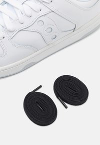White leather sneaker with black round laces laid flat below. Features include contrasting light blue accents and a textured design.