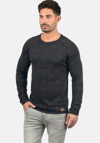 Maglione lungo a maniche lunghe di un blu navy testurizzato con scollatura rotonda. Presenta maniche raglan e una toppa in pelle marrone con logo sul fondo.
