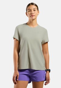 T-shirt de sport vert clair à manches courtes avec un col rond, des fentes sur les côtés et un logo discret sur la poitrine ; associé à un short violet.