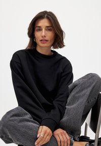 Zwarte crewneck sweatshirt, relaxte pasvorm, zachte stof, ribgebreide manchetten, gecombineerd met grijze high-waisted jeans, gladde textuur, minimale details.