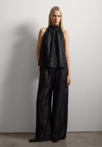 Top negro sin mangas con cuello alto y textura plisada, combinado con pantalones negros de pierna ancha y corte holgado. Tejido suave con un ligero brillo.