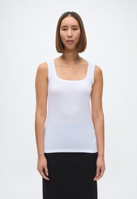 Balta topiņa bez piedurknēm, kas izgatavota no gluda, viegla auduma. Tai ir kvadrāta formas dekoltē un plata plecu lentes, ko papildina melna svārki.