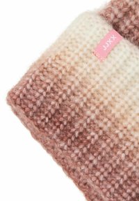 Stickad pannband med gradientfärger från brunt till kräm, med en liten rosa tygmärke med vit text.