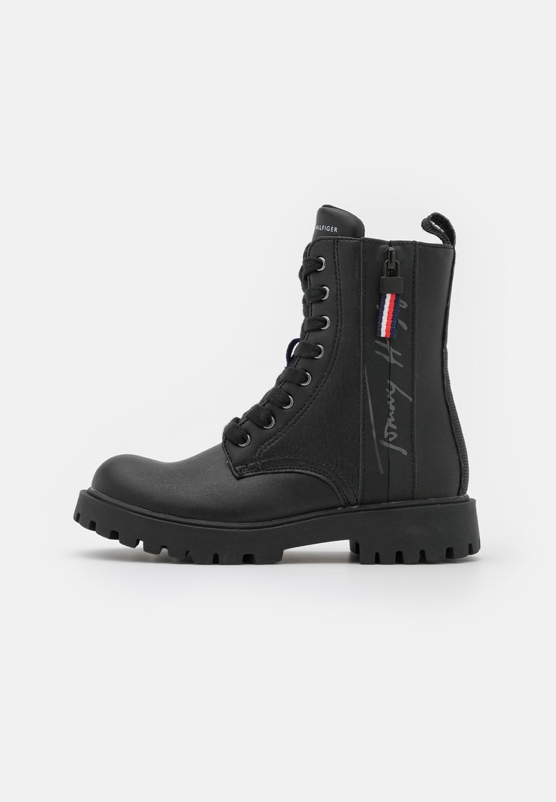 Botte de combat noire à lacets avec fermeture éclair latérale, semelle à crampons épaisse, languette de traction et logo Tommy Hilfiger sur le côté.