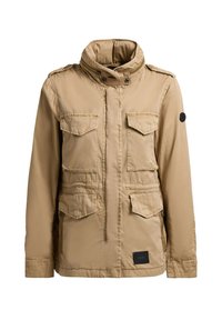 Giacca utilitaria marrone chiaro con colletto alto, quattro tasche frontali con patta, chiusura con zip e bottoni, e toppa con logo nero sulla parte anteriore inferiore.