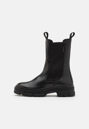 Bota negra de cuero hasta la mitad de la pantorrilla con paneles laterales elásticos, lengüetas de tirado en la parte delantera y trasera, y suela gruesa con textura para mayor agarre.