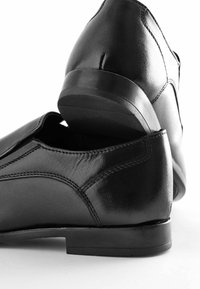 Schwarze Leder Schuhe mit glänzender Oberfläche, runden Zehen, minimalen Nähdetails und flachen Gummisohlen.