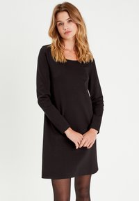 Vestido negro de manga larga con escote cuadrado, hecho de tela suave y elástica; diseño minimalista sin patrones o elementos metálicos visibles.